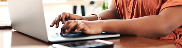 closeup view of the hands of a woman working at a computer on a desk.
