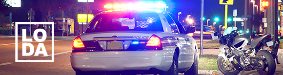 a rear view of a police car with lights flashing parked on the street next to a motorcycle with the LODA logo in the lower left corner