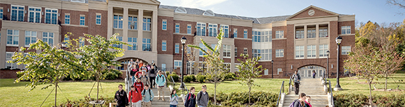 A large building at Radford University in Virginia with students walking and flower beds in the foreground.