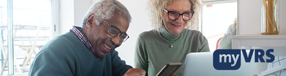 Decorative. An older man and woman smile while looking at a smart phone and a laptop computer screen. A home interior is in the background.