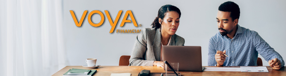 A woman and a man sit behind a desk in an office, looking at the screen of a laptop computer. A Voya sign is on the wall behind them.