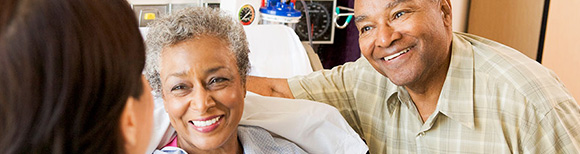 a woman in a hospital bed and a man standing next to her smile broadly at a woman in front of them.