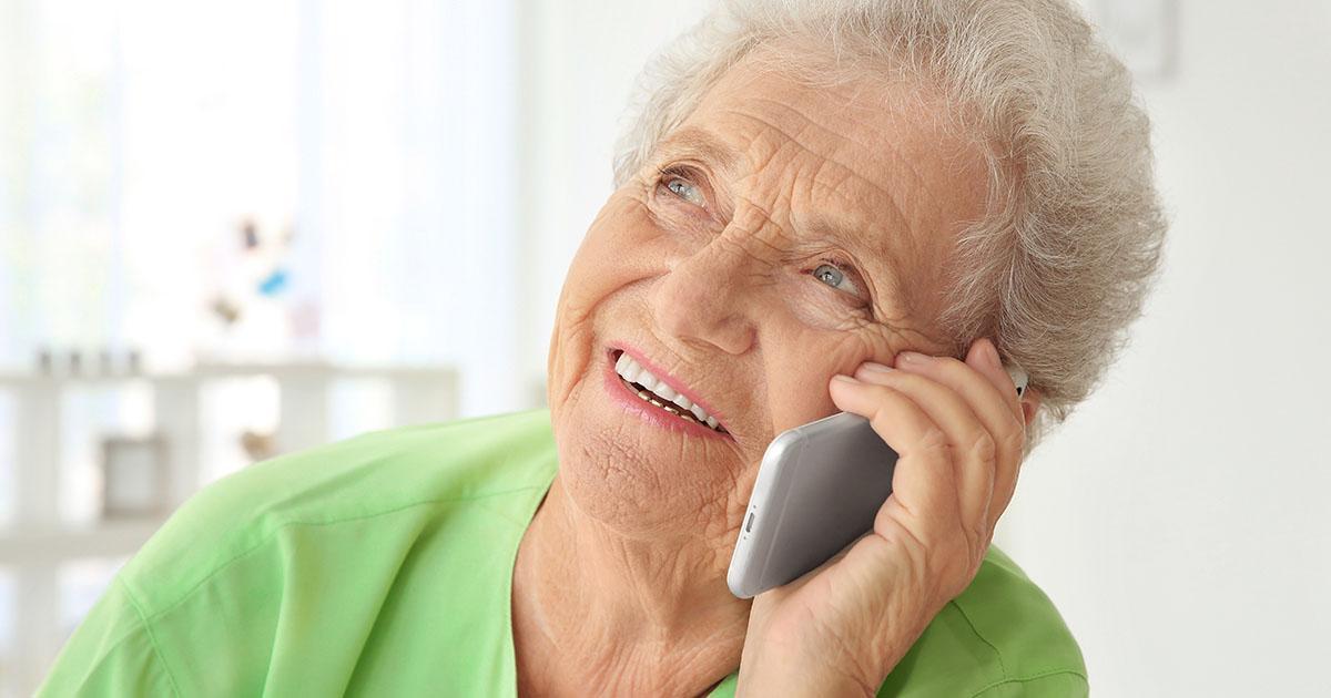 Decorative. An elderly woman smiles and looks upward as she listens to her phone at her ear.