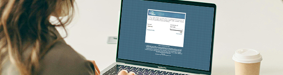 A woman seated at a desk looks at the VNAV login screen on her laptop.
