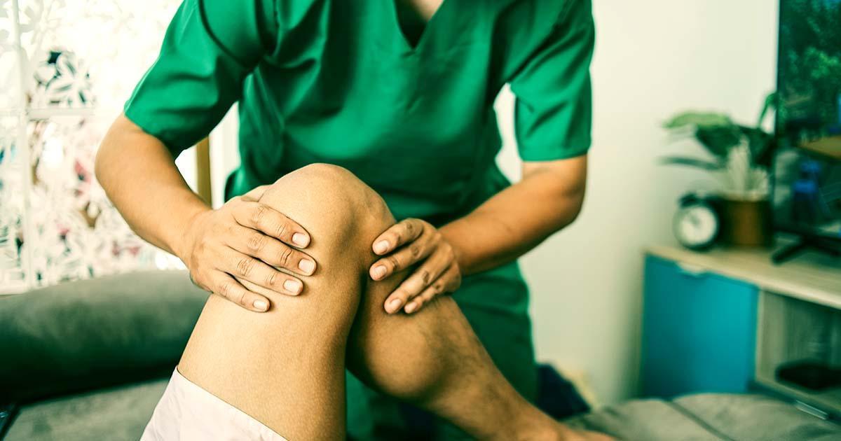 Decorative. Closeup view of a Physical Therapist wearing scrubs and working on a the left knee of a patient lying on a padded table.