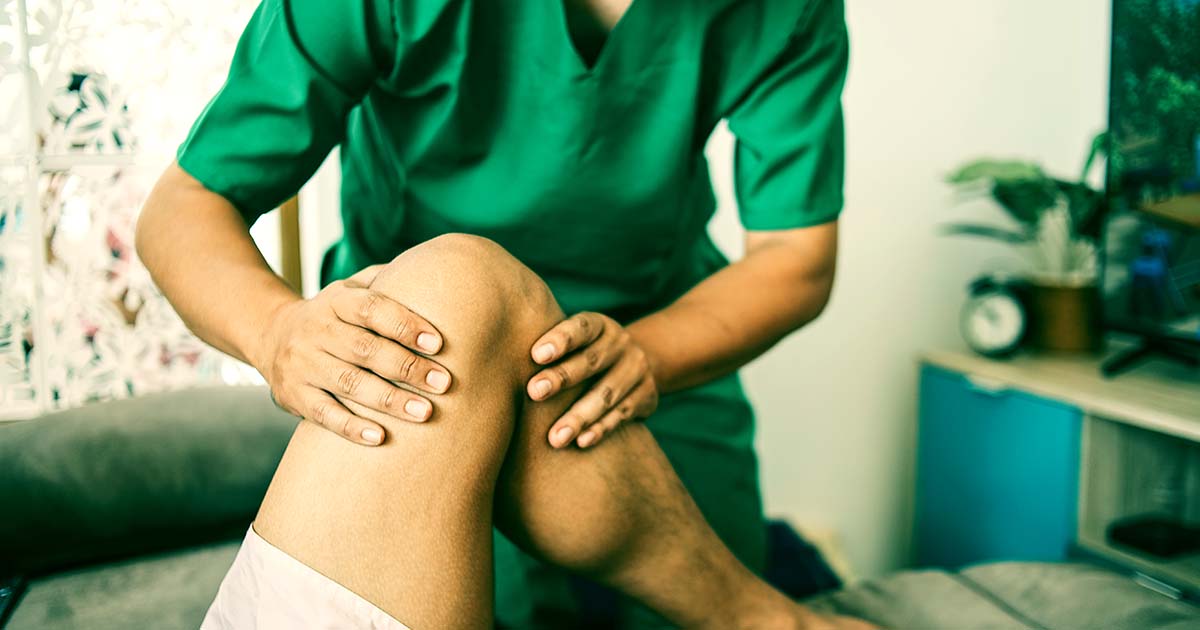 Decorative. Closeup view of a Physical Therapist wearing scrubs and working on a the left knee of a patient lying on a padded table.
