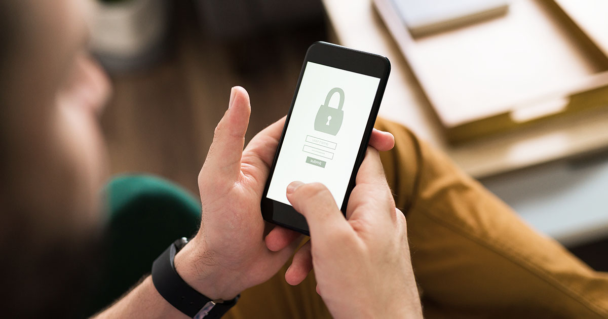 Decorative. Over-the-shoulder view of a person holding a smartphone in both hands. On the phone screen is a graphic of a padlock and a password field.