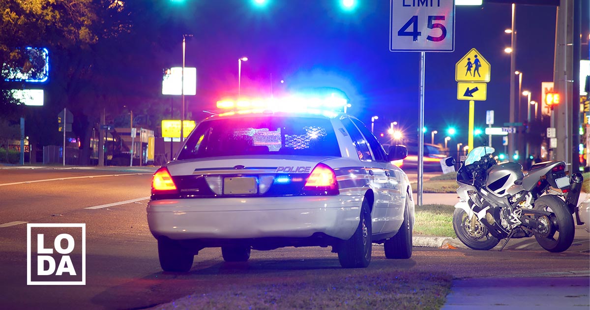A police cruiser parked on the side of an urban street at night. On the left is is LODA logo. Illustrative only.