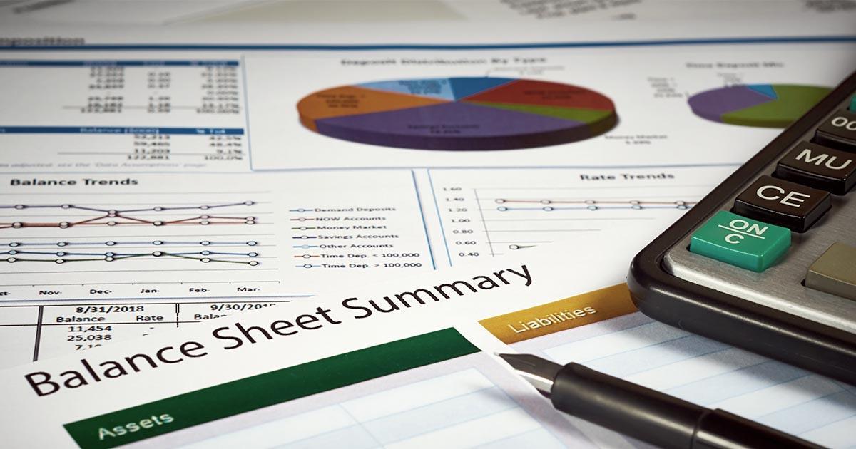 Decorative. Close-up view of financial papers with charts and graphs on a table surface with a fountain writing pen in the foreground. The paper in the foreground is titled Balance Sheet Summary.