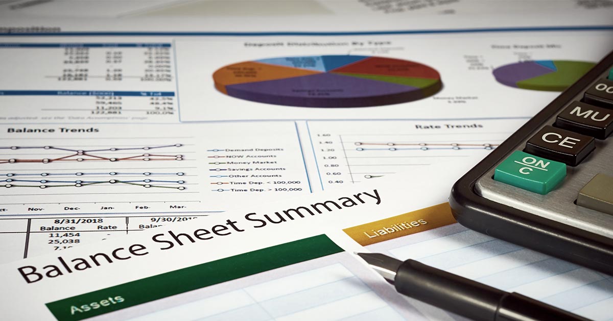 Decorative. Close-up view of financial papers with charts and graphs on a table surface with a fountain writing pen in the foreground. The paper in the foreground is titled Balance Sheet Summary.
