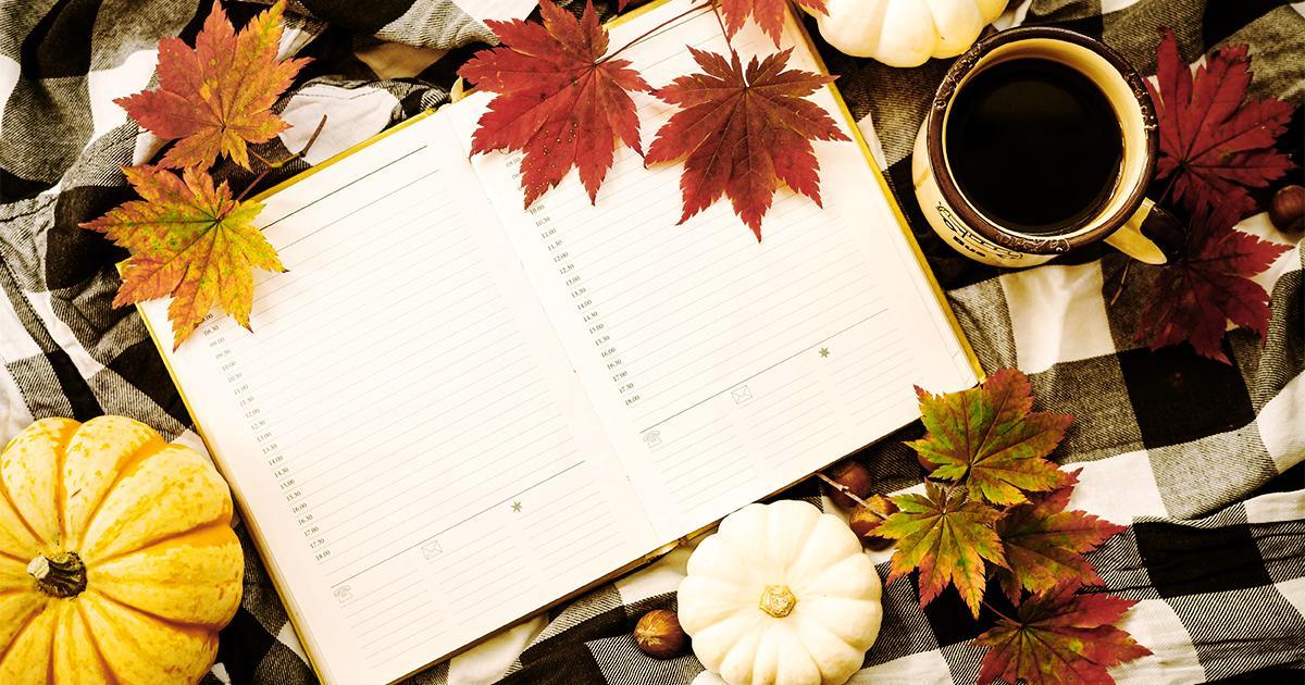 Illustrative. An open planner book showing dates and room to write lying on a background of plaid patterned fabric and autumn leaves.