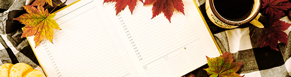 Illustrative. An open planner book showing dates and room to write lying on a background of plaid patterned fabric and autumn leaves.