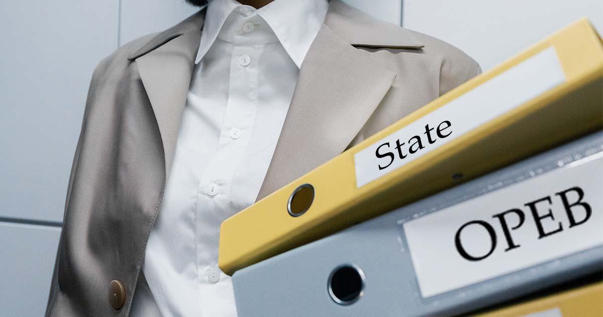 Decorative. A female torso in professional dress holds two loose leaf binders in the left hand. Labels on the spines of the binders read State and OPEB. A tiled wall is in the background.