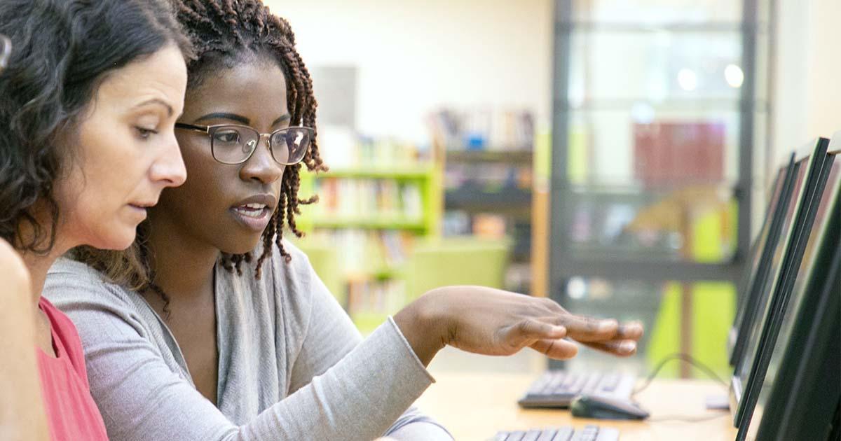 Decorative. A woman gives instruction to another woman and a man looking over her shoulder at a computer screen.