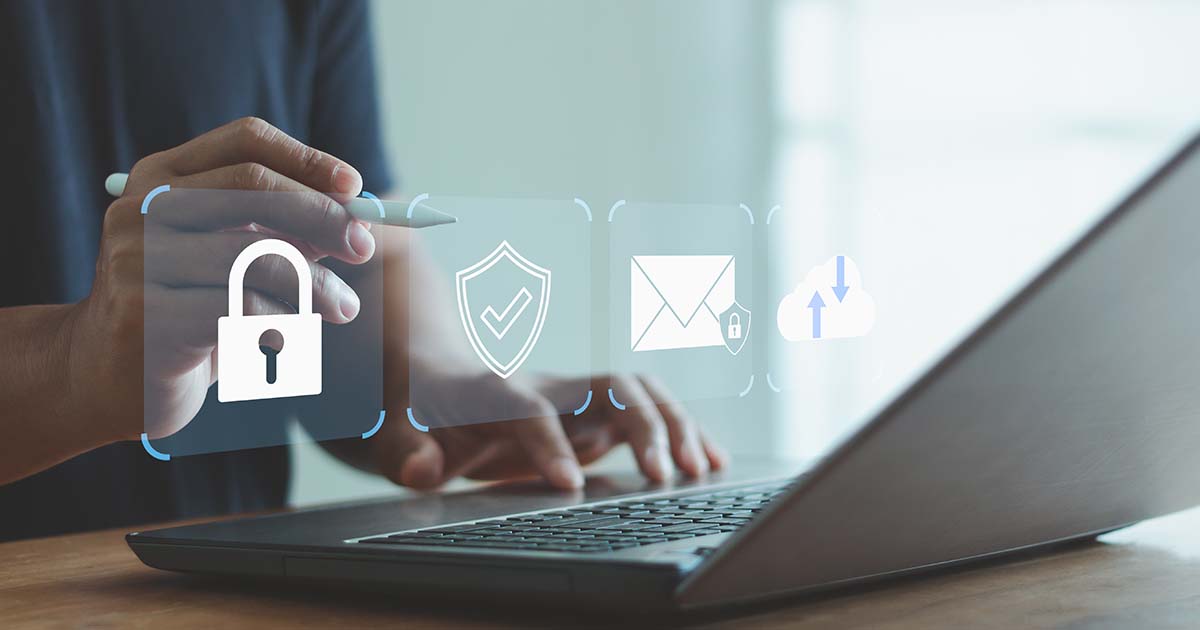Decorative. On the left, a man's hand touches his phone which is lying on a table. Above the phone is a superimposed graphic of a shield and padlock to illustrate email encryption security. Just beyond the phone, a pair of eyeglasses rests on the table. To the right of the frame, a coffee cup with coffee in it sits on the same table.