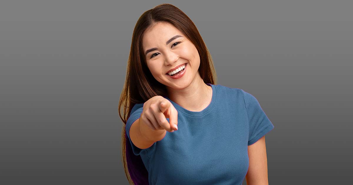 Decorative. A young, smiling woman tilts her head and points at the viewer.