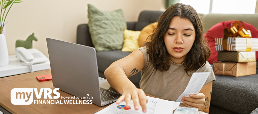 A person working on a computer and reviewing bills and financial papers.