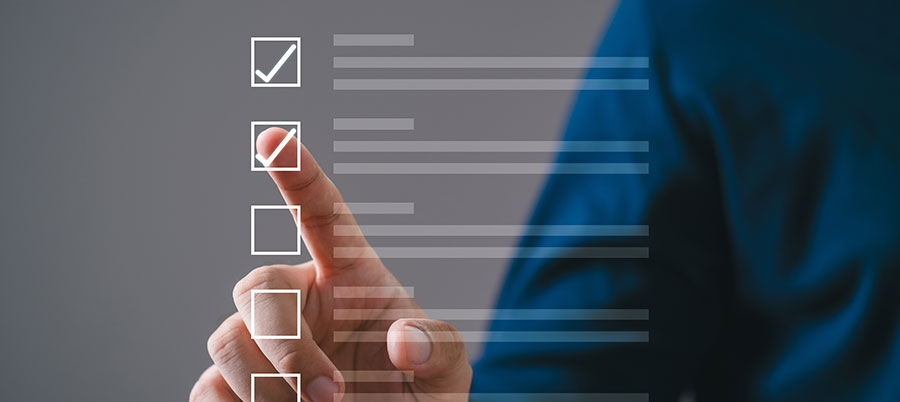 Photograph showing a person’s hand selecting a checkbox on a transparent digital checklist interface with multiple options. The image highlights interaction with digital forms, featuring white checkboxes and text lines against a blurred gray and blue background.